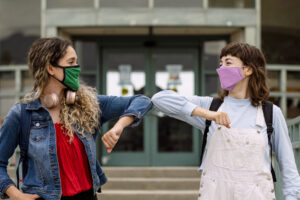 Female students wearing masks shacking hands by touching elbows.