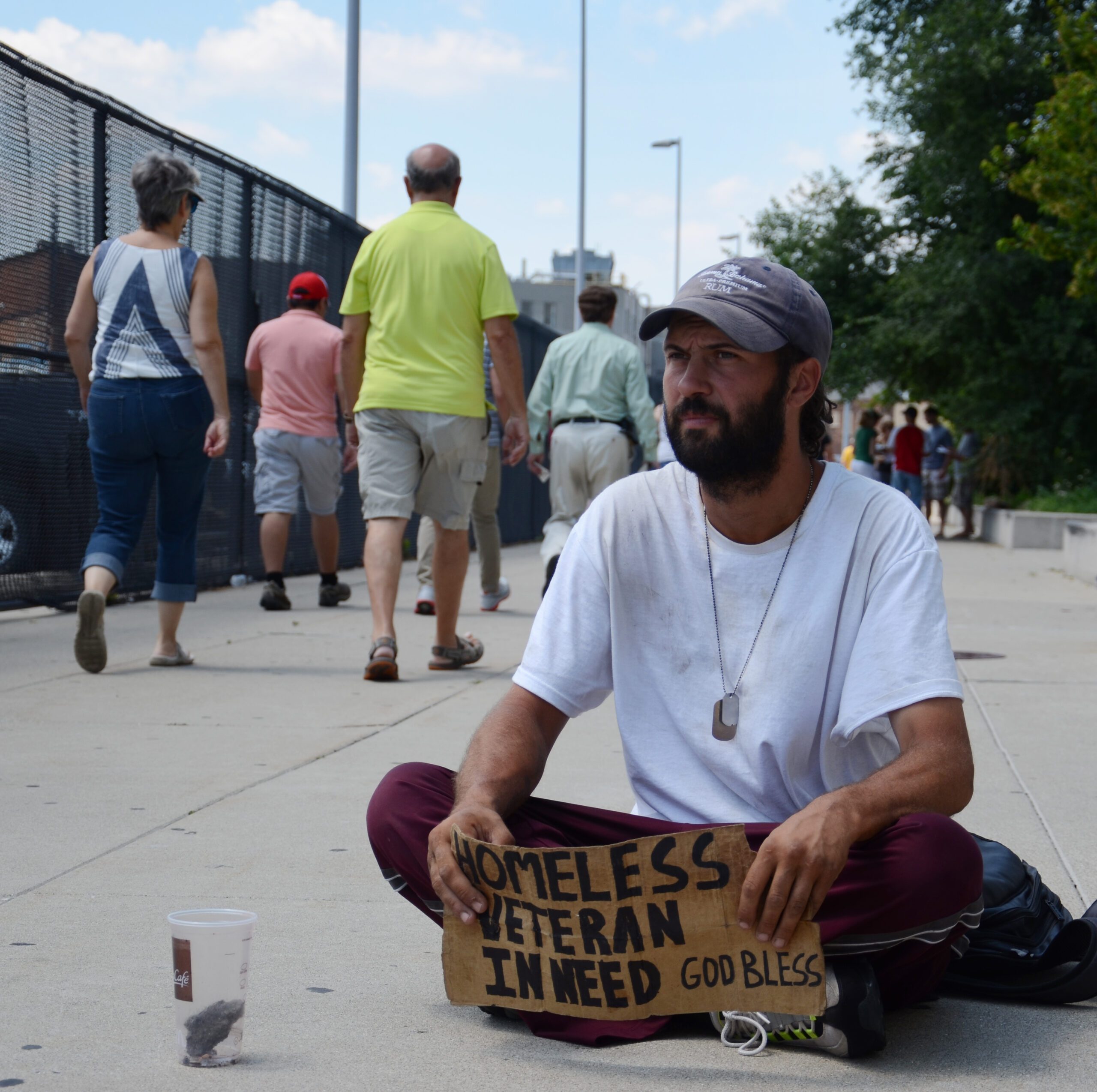 A homeless veteran asking for help on the street as people walk by.