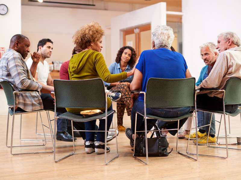 A diverse group sitting in chairs in a circle talking to each other and showing support.